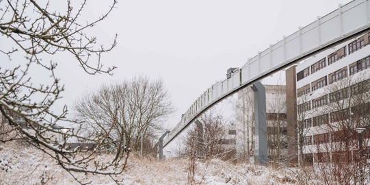 Campus Nord im Winter Verschneiter Nordcampus mit einem Gebäude, der H-Bahn-Strecke und Bäumen.