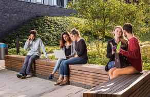 Studierende auf dem Campus Studierende sitzen auf einer Sitzgruppe hinter dem neuen Physikgebäude