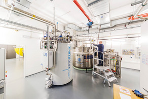 Innenaufnahme Labor Kyrotechnik Ein Labor mit einem großen weißen Behälter für Kyrotechnik und einem Metallbehälter, ein Mann steht auf einer Leiter.