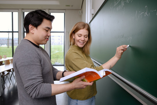 Zwei Studierende an der Tafel Zwei Studierende an der Tafel, er hält Buch, sie schaut rein, beide lächeln